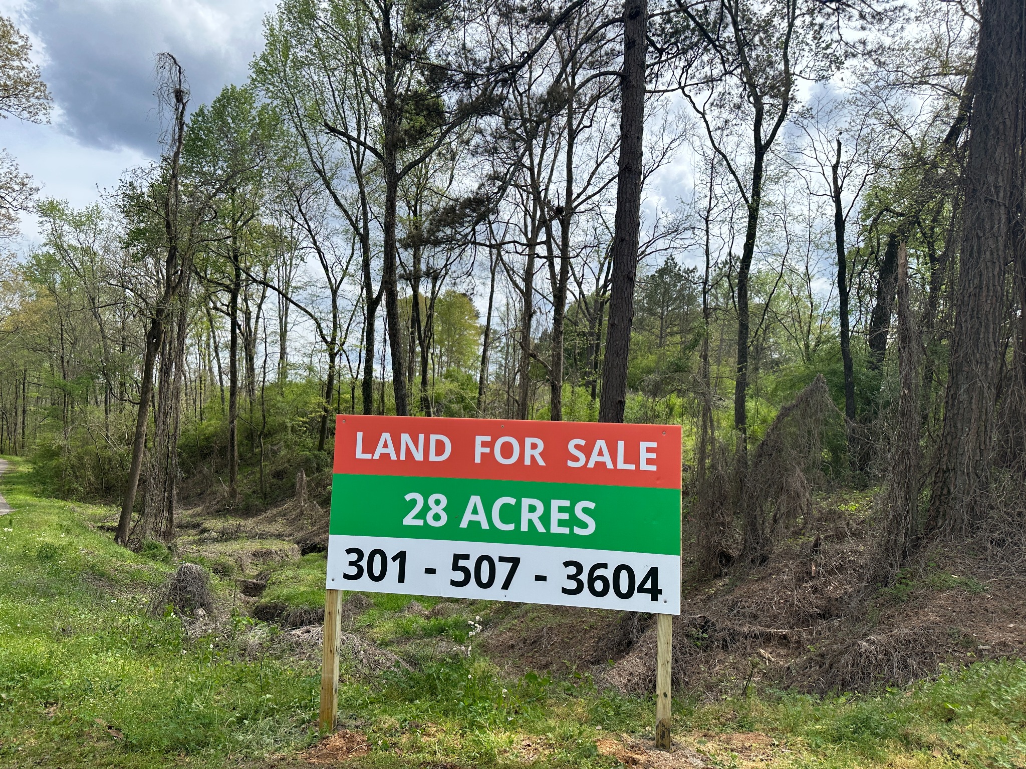 Roadside land for sale sign advertising 28 acres with contact phone number